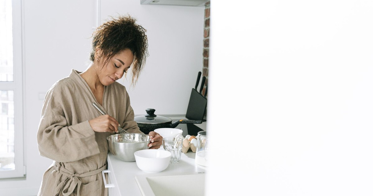 A young woman prepares food in a stylish white kitchen, mixing ingredients in a bowl.