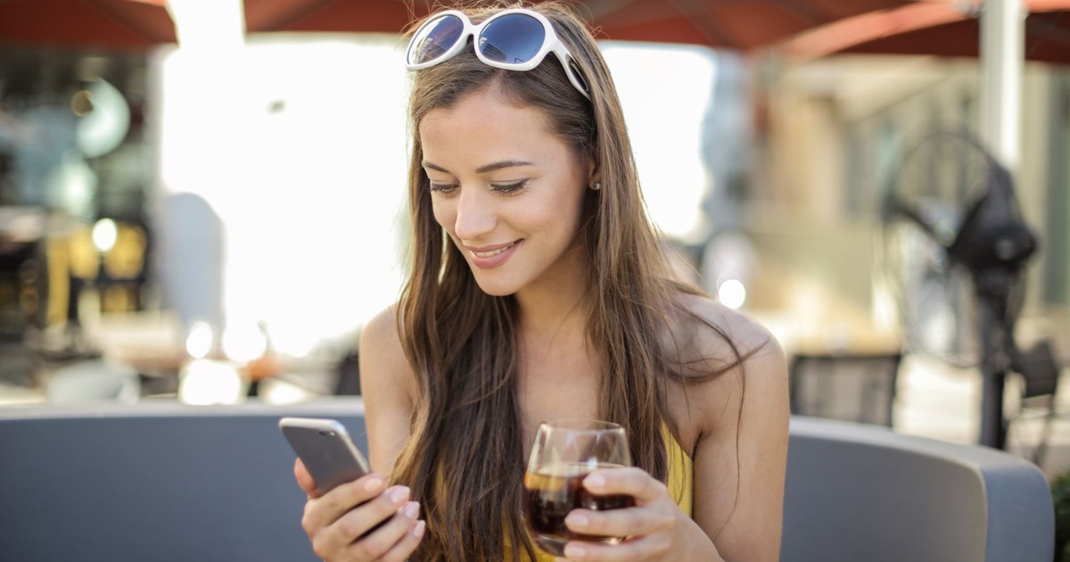 Smiling woman with a drink and smartphone outdoors enjoying leisure time happily.