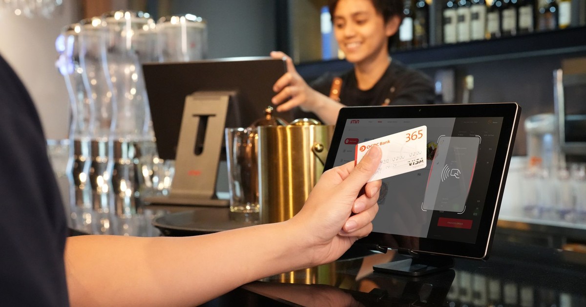 Person using contactless credit card payment at a modern bar, assisted by a cashier.