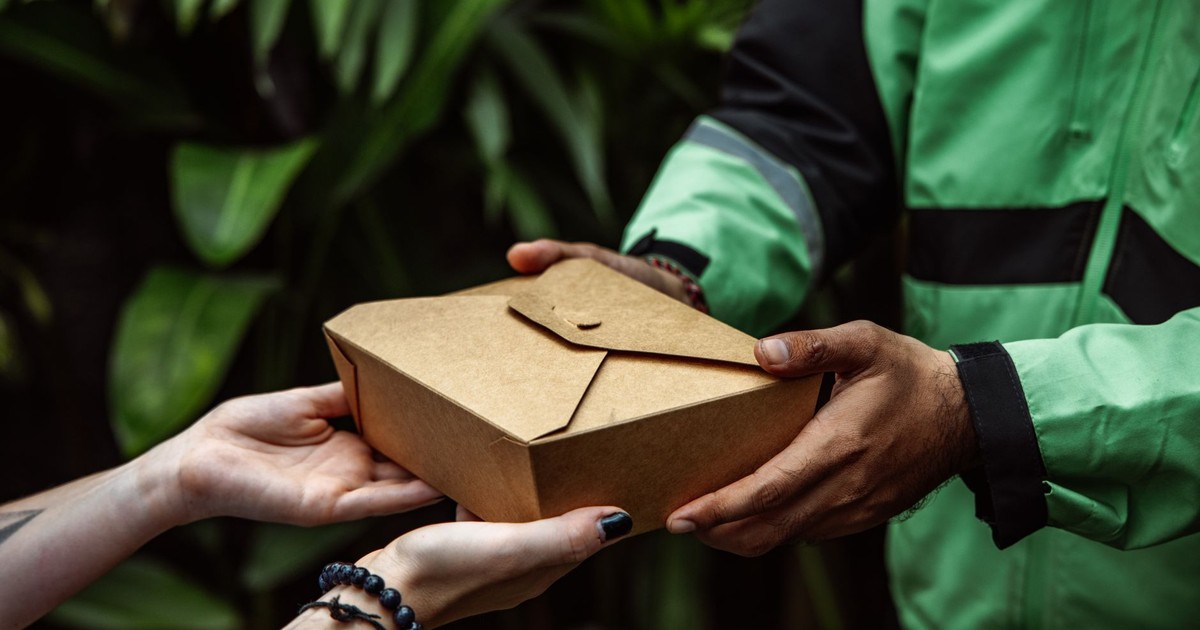Close-up of hands exchanging an eco-friendly takeout box outdoors.