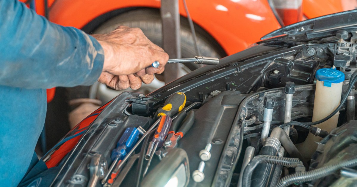 Mechanic performing maintenance on a car engine in a garage setting, using various tools.