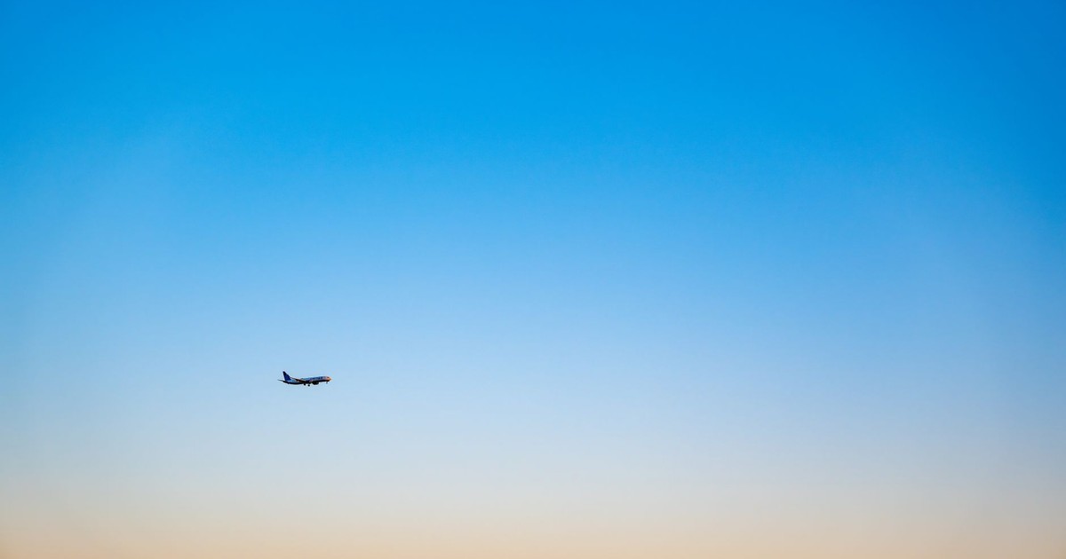 A lone airplane flying in a gradient blue and orange sky during sunset, creating a serene travel backdrop.