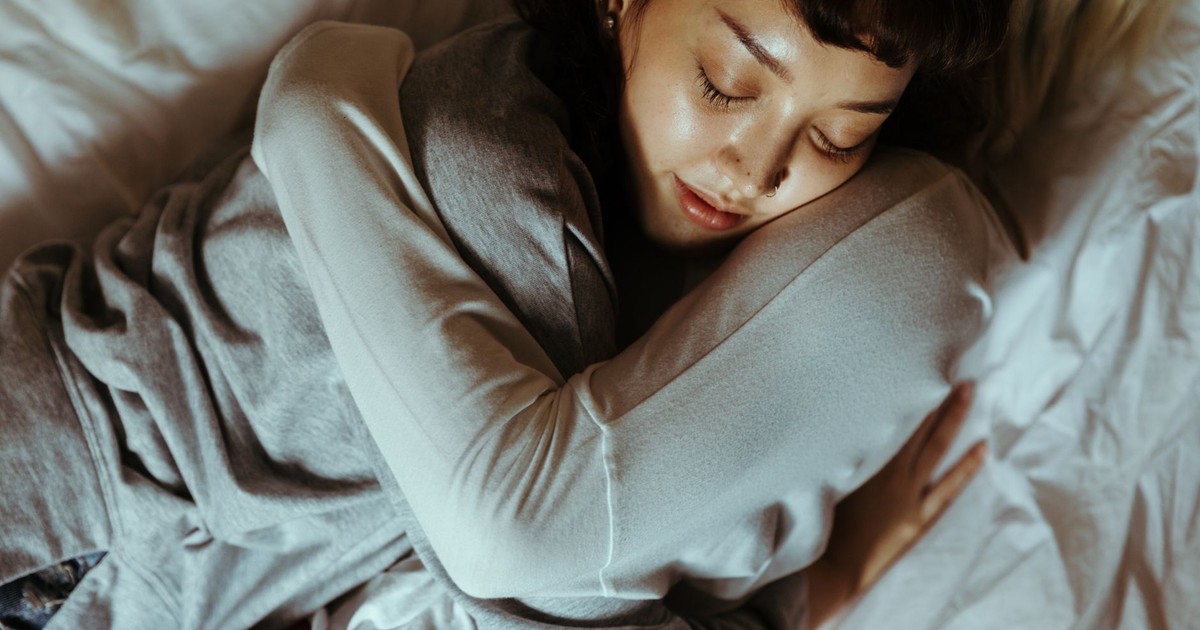 From above of young women lying on bed and sleeping while hugging each other and sleeping together during weekend at home