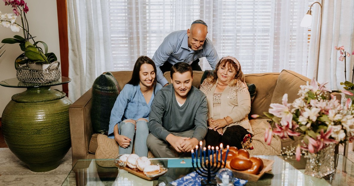 A joyful family celebrating Hanukkah with lit menorah, challah, and sufganiyot indoors.