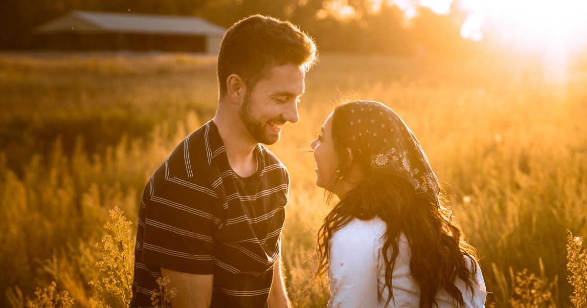 A joyful couple shares a moment in a sunny field at sunset, radiating warmth and happiness.