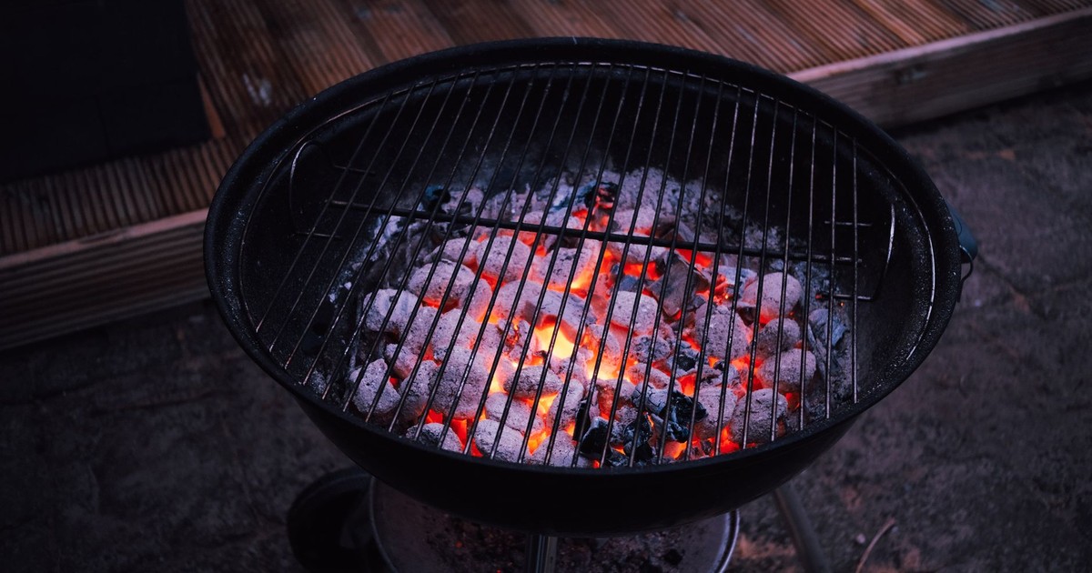 Close-up of glowing charcoal briquettes in a round outdoor grill, ready for barbecue cooking.