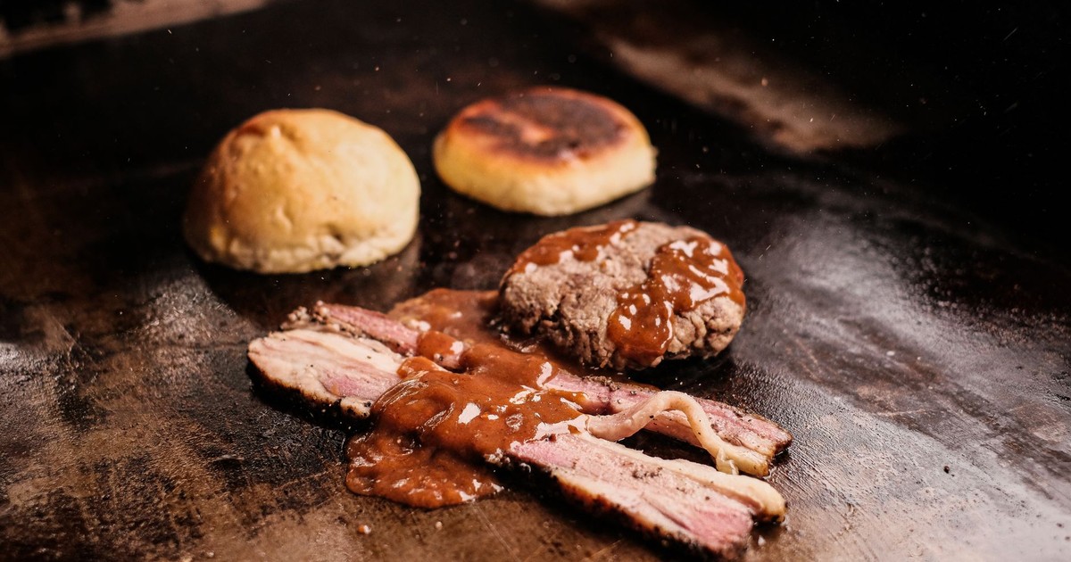Close-up of grilled meats with savory sauce and buns, sizzling on a hot grill. Captures the essence of barbecue.