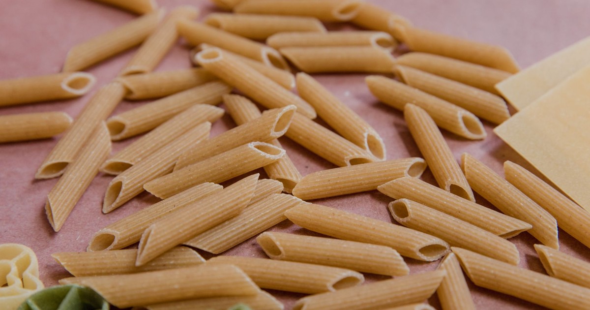 Detailed image of uncooked penne and other pasta on a pink background.