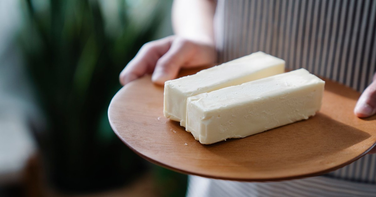 Close-up of hands holding a wooden plate with two sticks of butter.