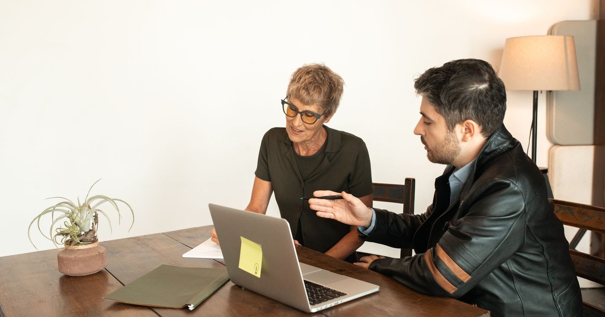Senior woman and adult man collaborating over a laptop while seated indoors.