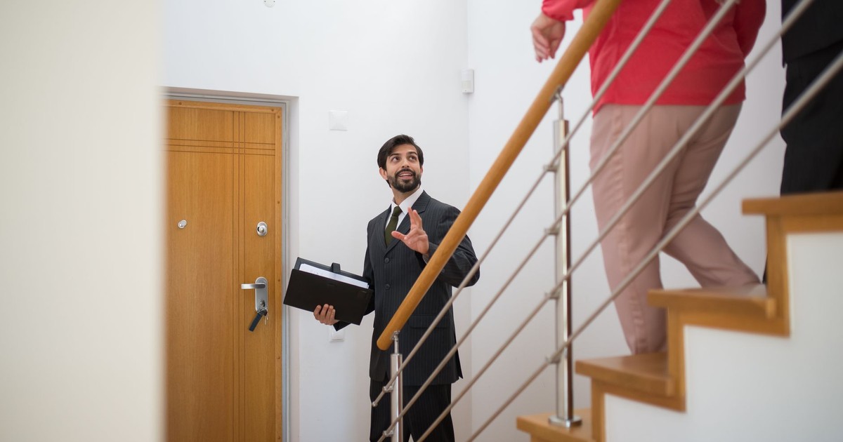 A realtor conducting a house tour with potential buyers on the stairs of a modern home.