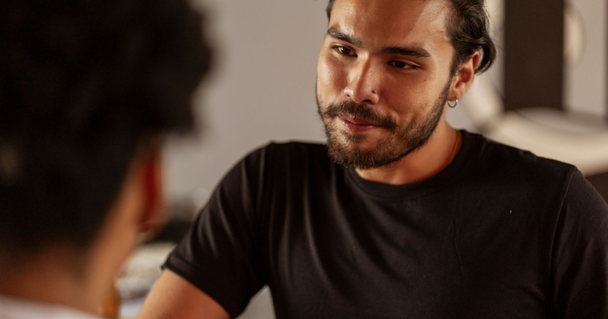 A bearded man attentively engaged in a conversation indoors, wearing a black shirt.