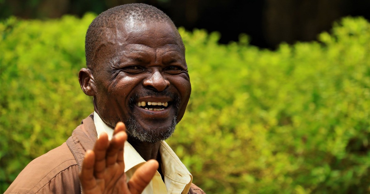 African man smiling joyfully in a vibrant green outdoor setting in Uganda.