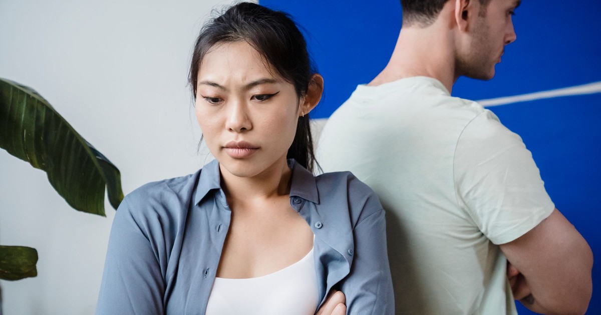 A couple in disagreement standing back to back with crossed arms, indoors.