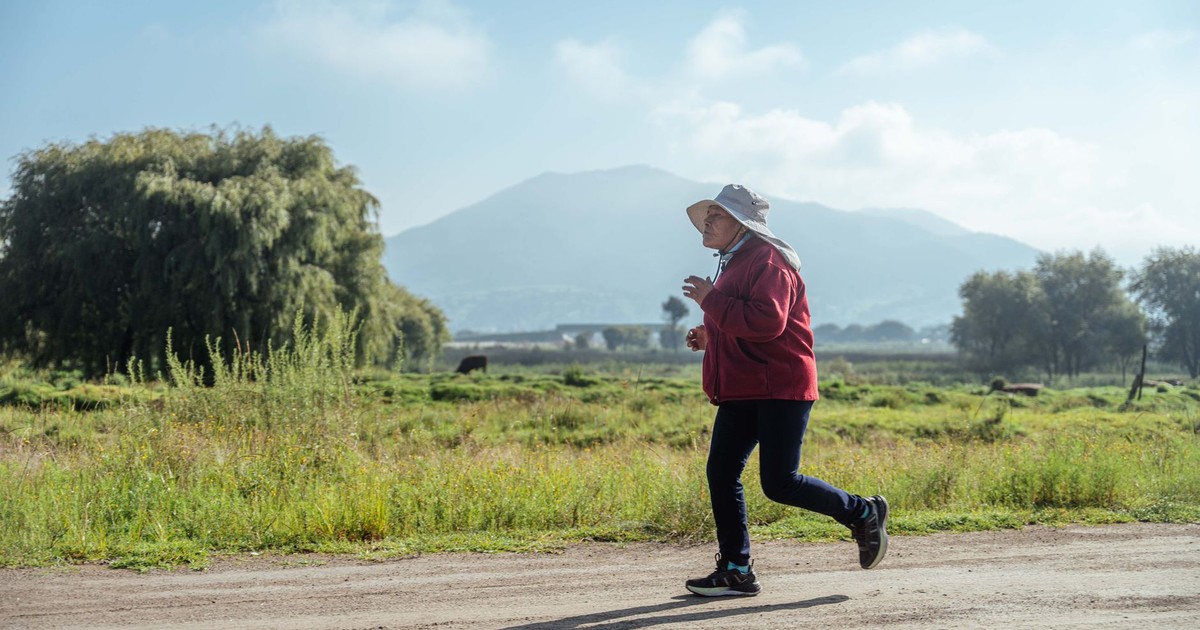Senior woman jogging on a dirt road in a rural landscape with mountains in the background.