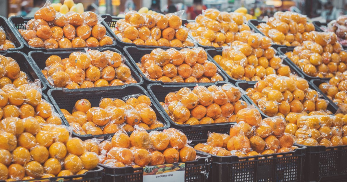 Stack of fresh oranges wrapped in plastic at a grocery store, priced with tags.