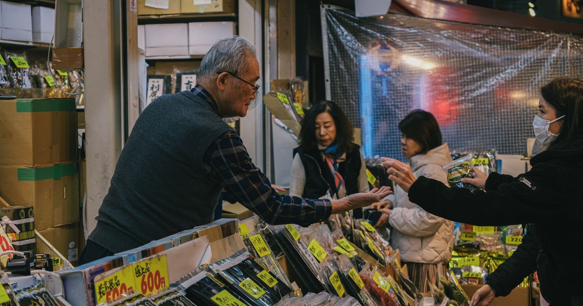 A scene in a bustling Japanese market with shoppers and a vendor engaging in transactions.