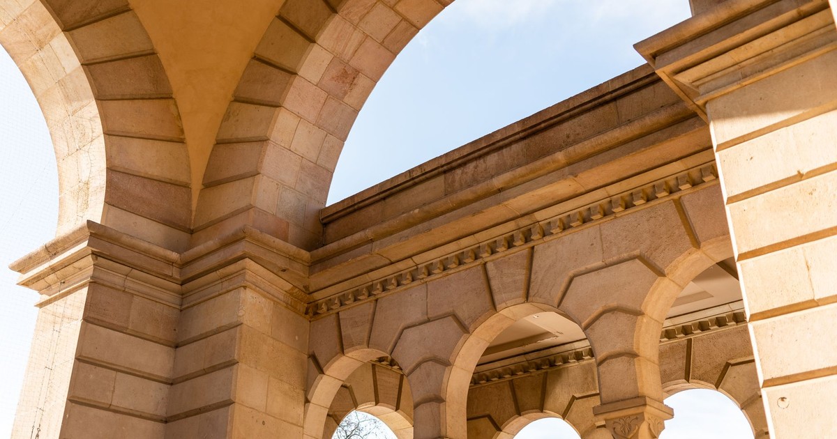 Low angle of stone historic building with arch and columns under blue sky