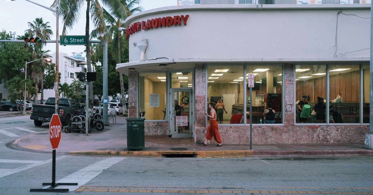 Laundromat on a city corner with pedestrians passing by on a sunny day.