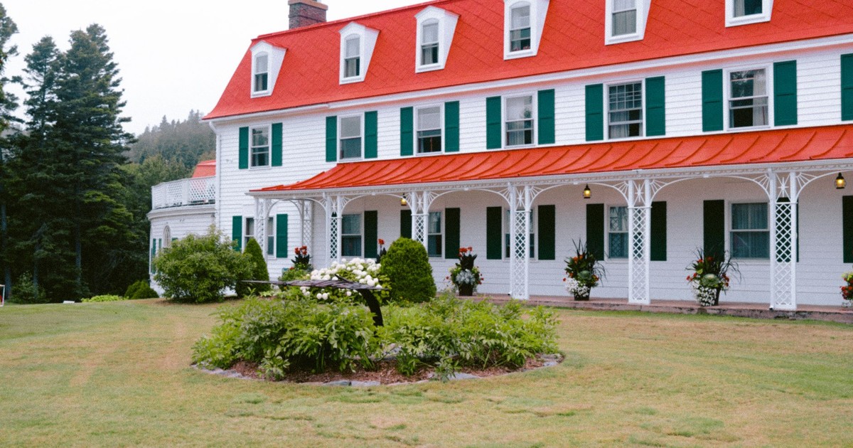 Classic hotel exterior with red roof, white facade, vibrant garden, and surrounding trees.