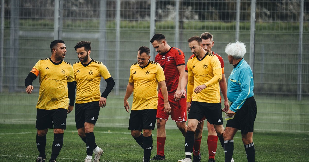 Amateur soccer players in yellow uniforms and referee on the field after a match.