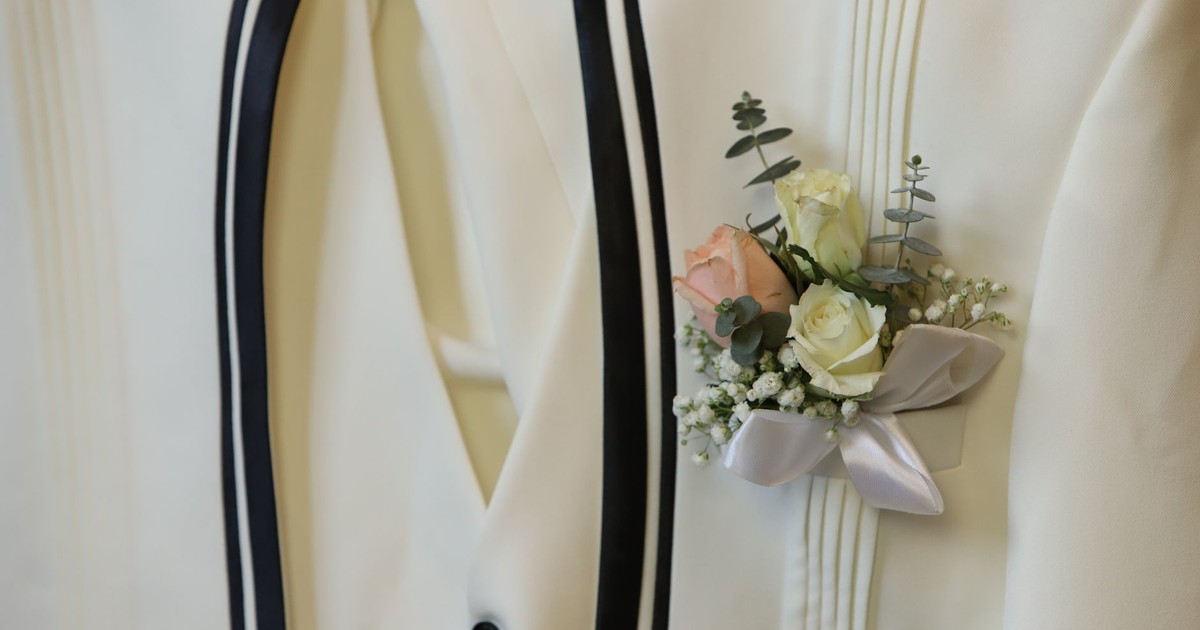 Detailed close-up of an elegant white suit adorned with a floral boutonniere, ideal for wedding photography.