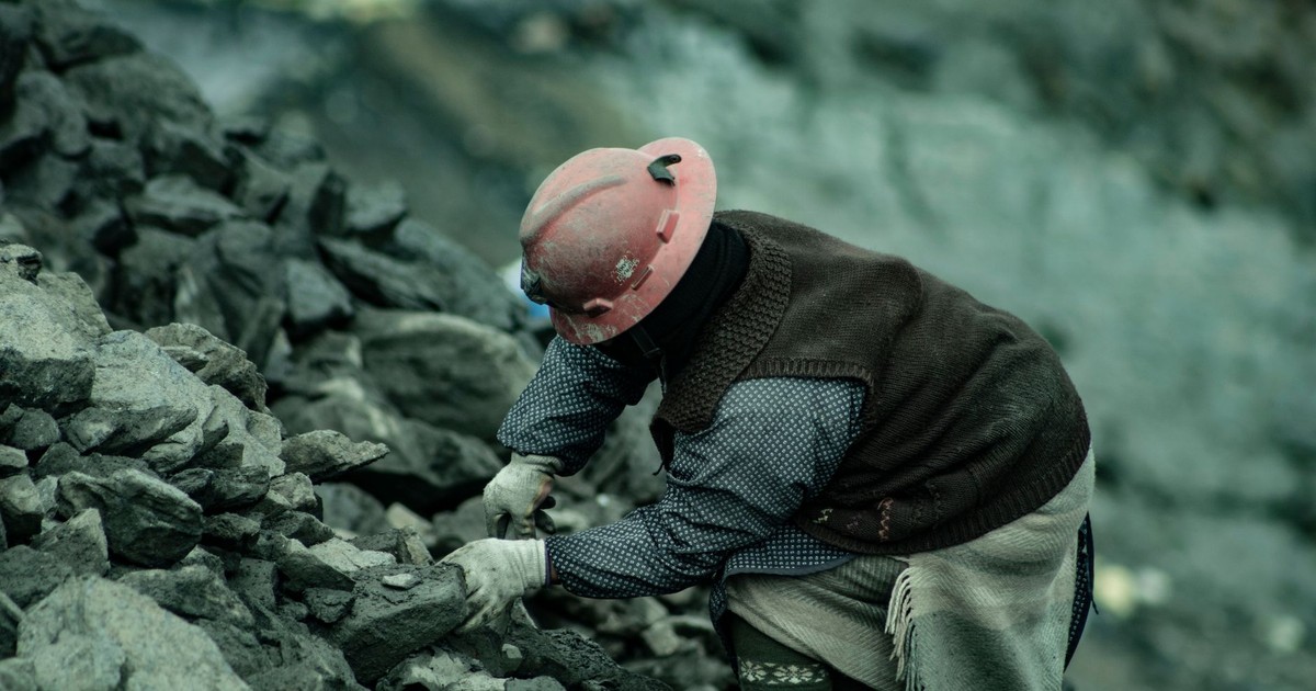 A coal miner in a hard hat working amidst rocky terrain, emphasizing labor and resilience.