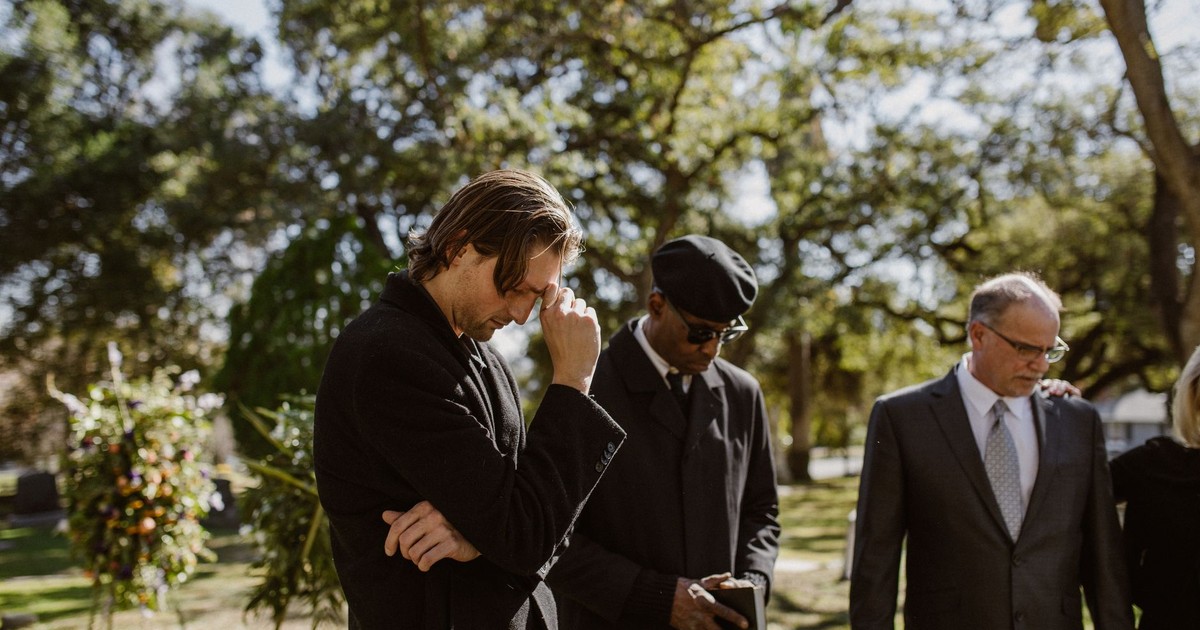 Group of mourners in formal wear attending an outdoor funeral.