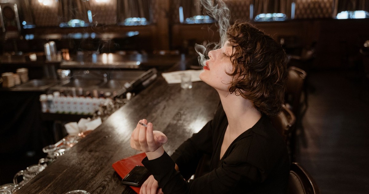 A woman in a black dress elegantly smokes at a vintage bar, exuding a classic and cinematic allure.