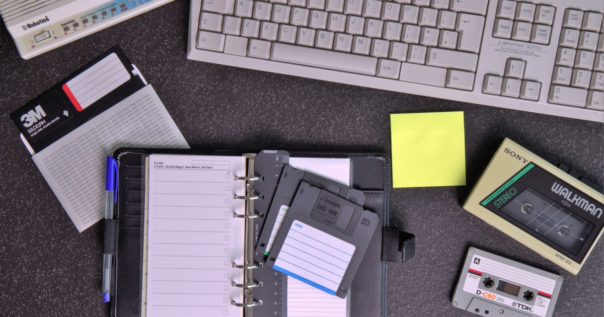 Flat lay of retro office supplies featuring a Walkman, floppy disks, keyboard, and planner.