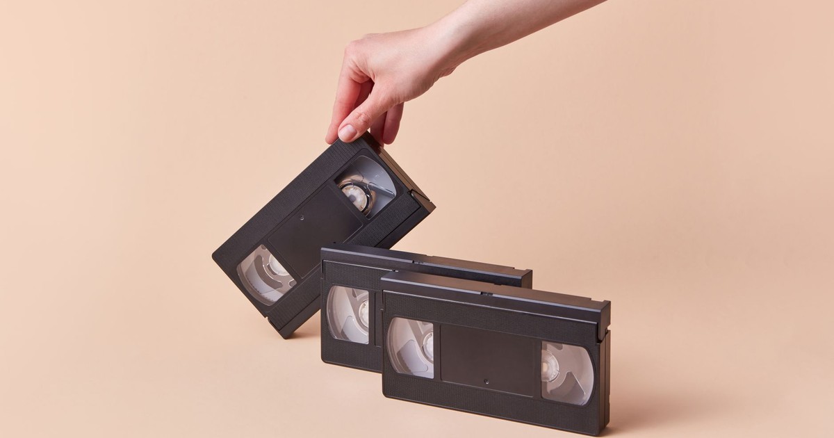 Hand holding a vintage VHS tape with a retro collection against a beige background.