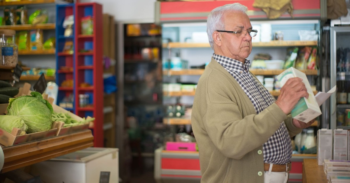 Senior man in a cardigan browsing products in a Portuguese grocery store.