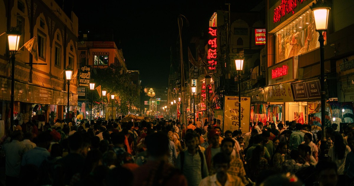 A bustling street in Varanasi, India, illuminated at night with crowds and vibrant signs.
