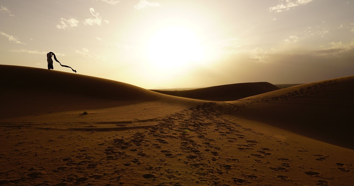 Silhouette of a person in Drâa-Tafilalet desert, Morocco during a striking sunset scene, creating dramatic shadows.