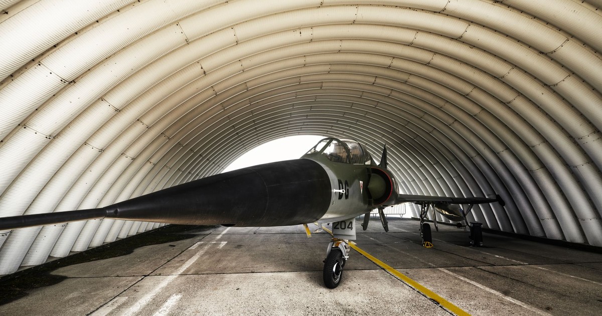 A fighter jet parked inside an arched military hangar, showcasing its sleek design.