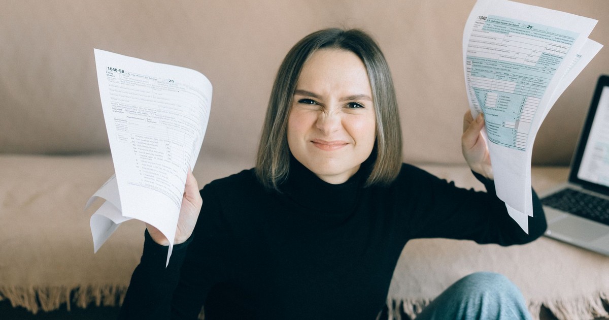 Frustrated young woman holding tax documents while sitting indoors.