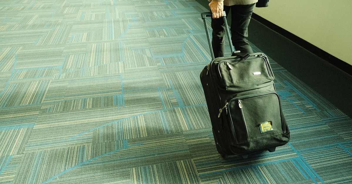 Person walking with luggage on blue carpeted airport corridor, traveling