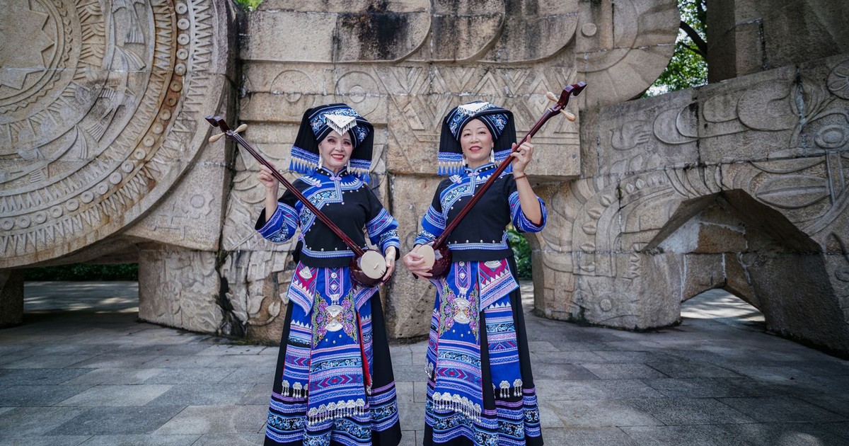 Two women in traditional Zhuang costumes playing musical instruments outdoors.