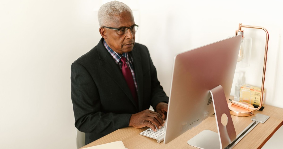 Senior man in corporate attire focusing on work at his desktop computer in a modern office.
