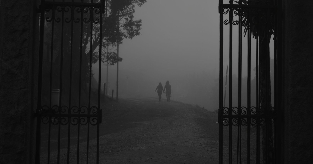 Two people walk hand in hand through a foggy open gate, creating a moody silhouette.