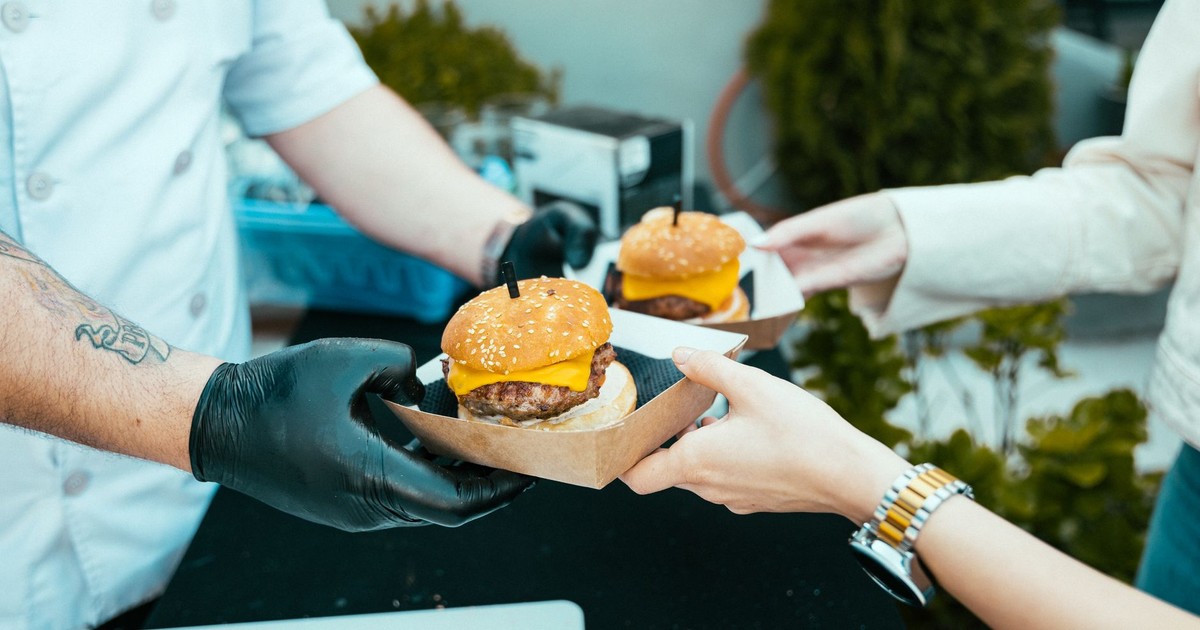 Chef hands over delicious cheeseburgers to a customer at an outdoor food stall.