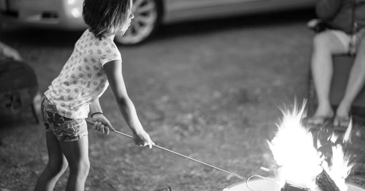 A young girl roasts marshmallows over an outdoor campfire at dusk.