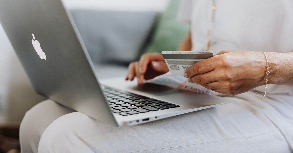 Close-up of a person holding a credit card while shopping online using a laptop at home.