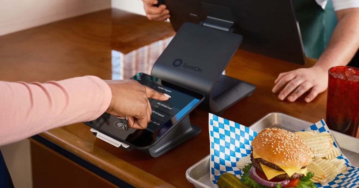 Restaurant counter with SpotOn POS system and burger meal, featuring customer interaction.