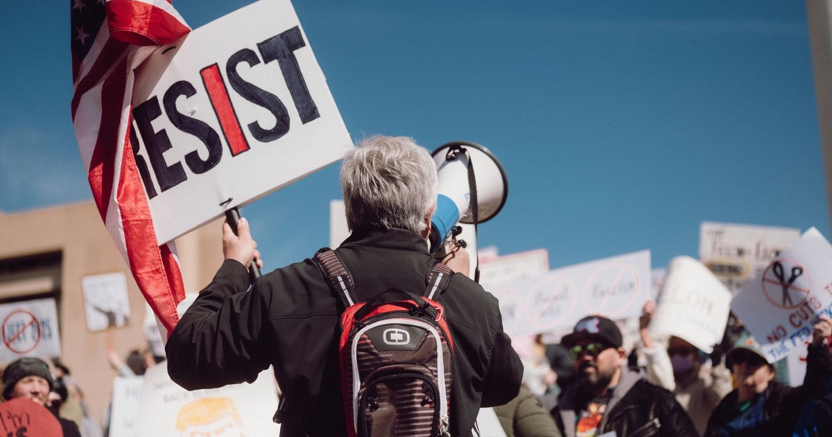 Crowd at a rally holding signs with a strong message of resistance.