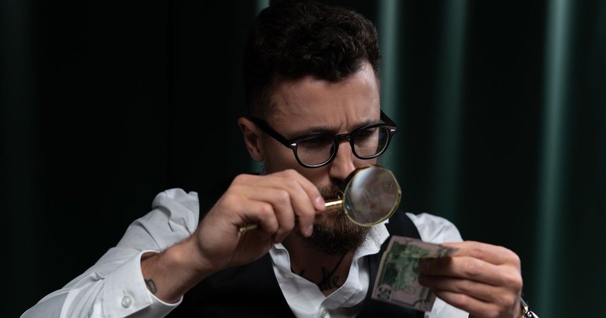 Focused adult inspecting a banknote closely with a magnifying glass indoors.