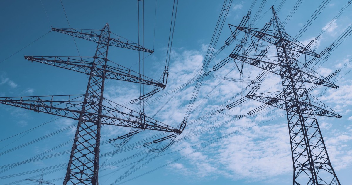 High voltage transmission towers stretch across a clear blue sky, symbolizing energy and industry.