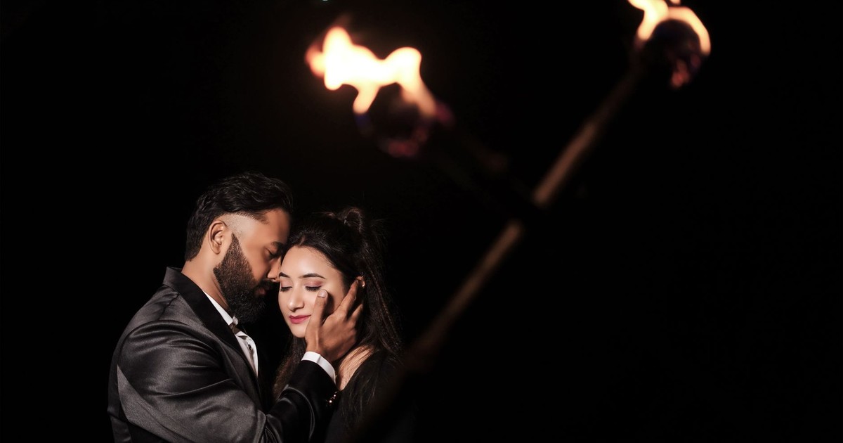 A romantic couple embraces under burning torches against a dark backdrop.
