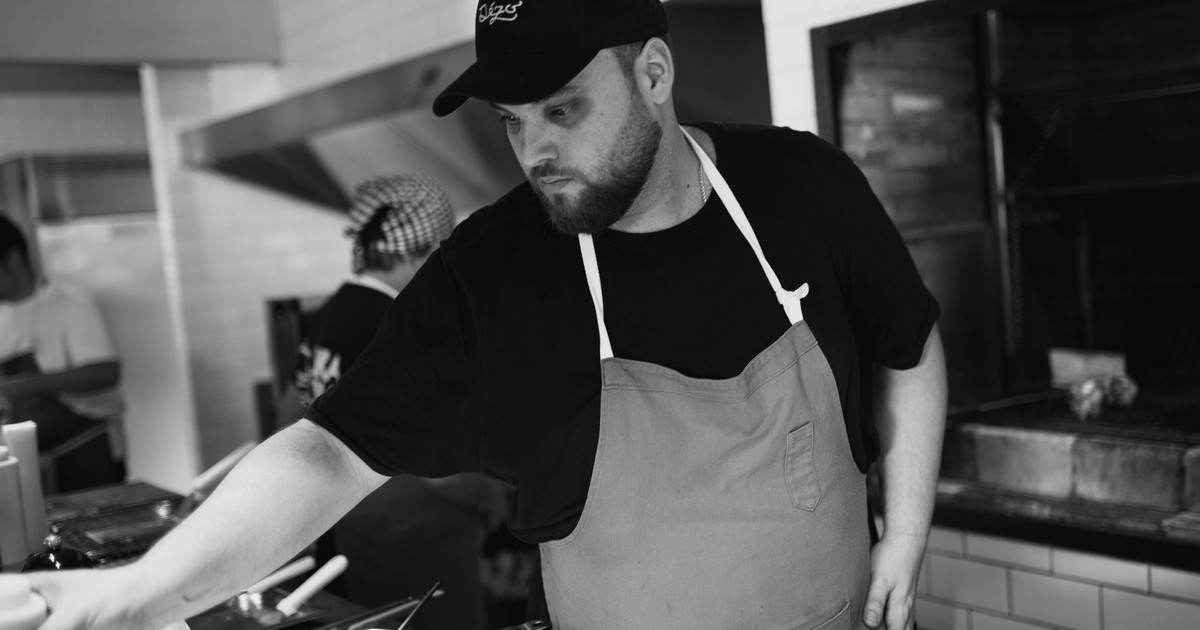 A focused chef working in a professional kitchen, wearing an apron and cap.