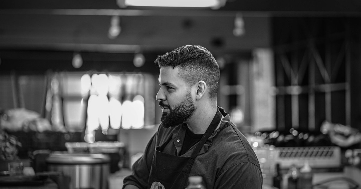 Black and white photo of a bearded chef at work in a kitchen environment.